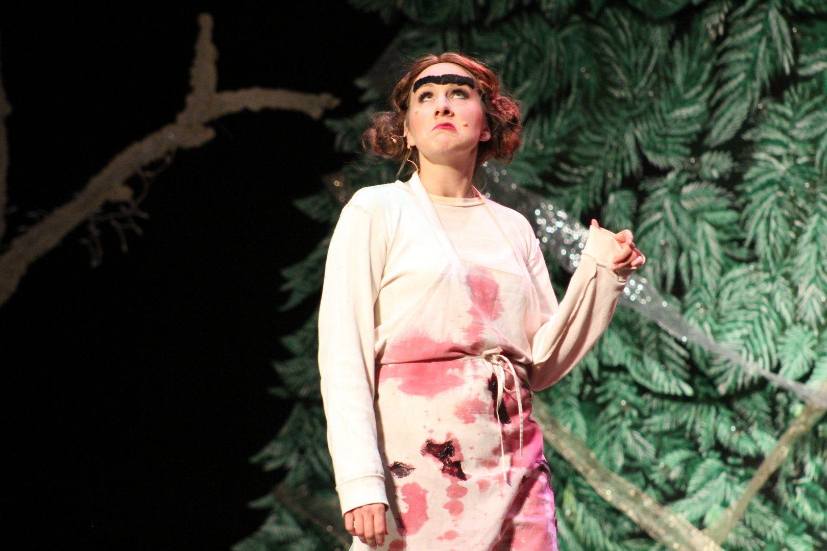 A woman in a pink dress is standing on a stage in front of a tree.