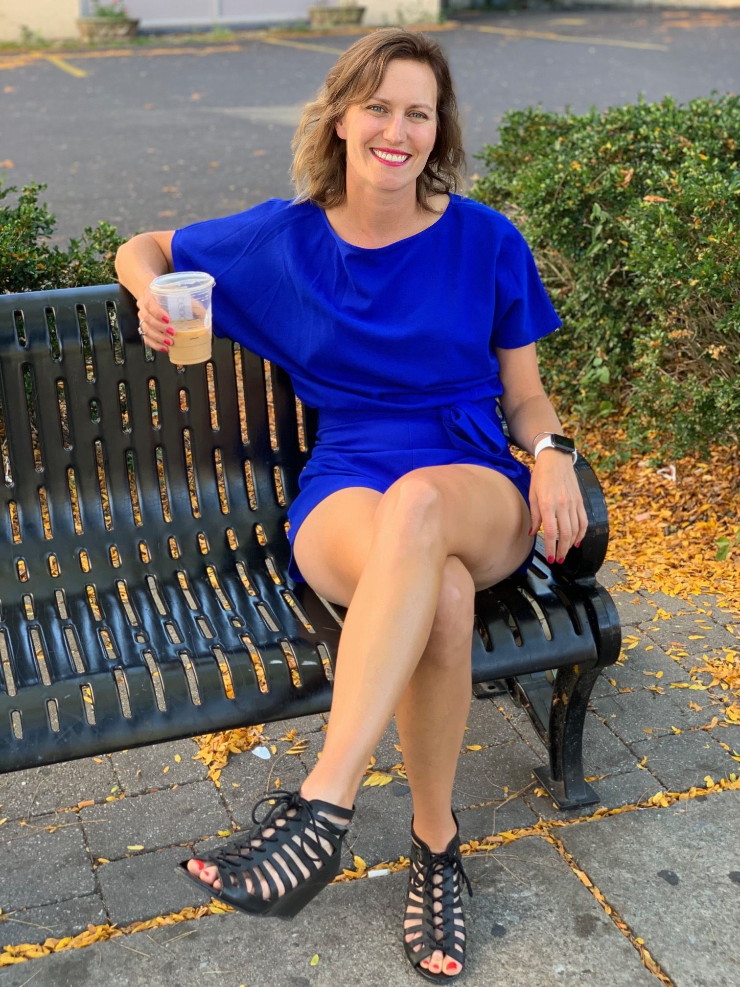A woman in a blue dress is sitting on a bench holding a cup of coffee.