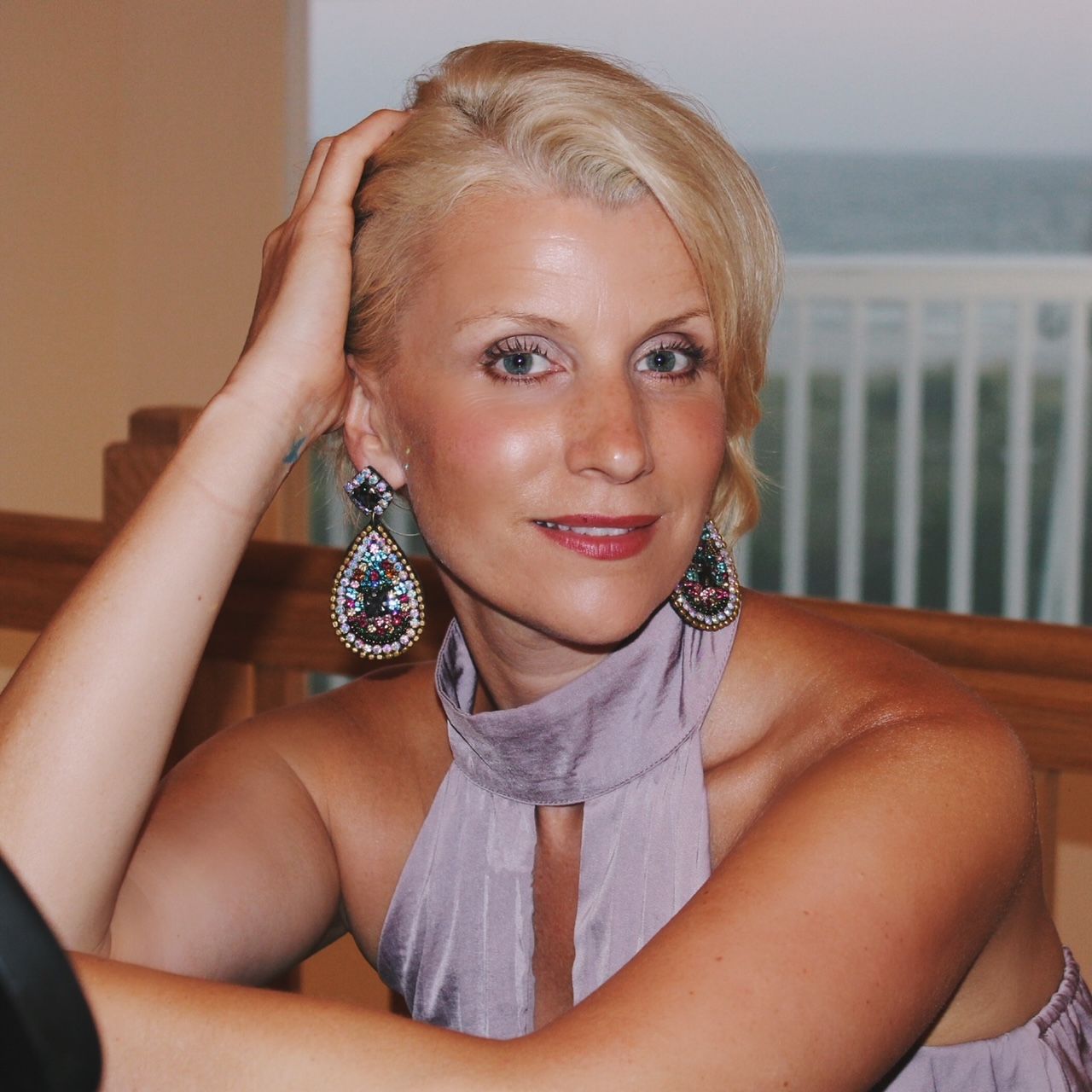 A woman wearing a purple dress and earrings holds her hand to her head