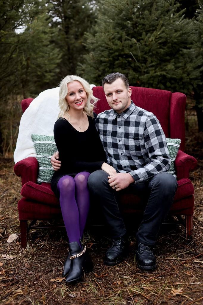 A man and a woman are sitting on a red couch in the woods.