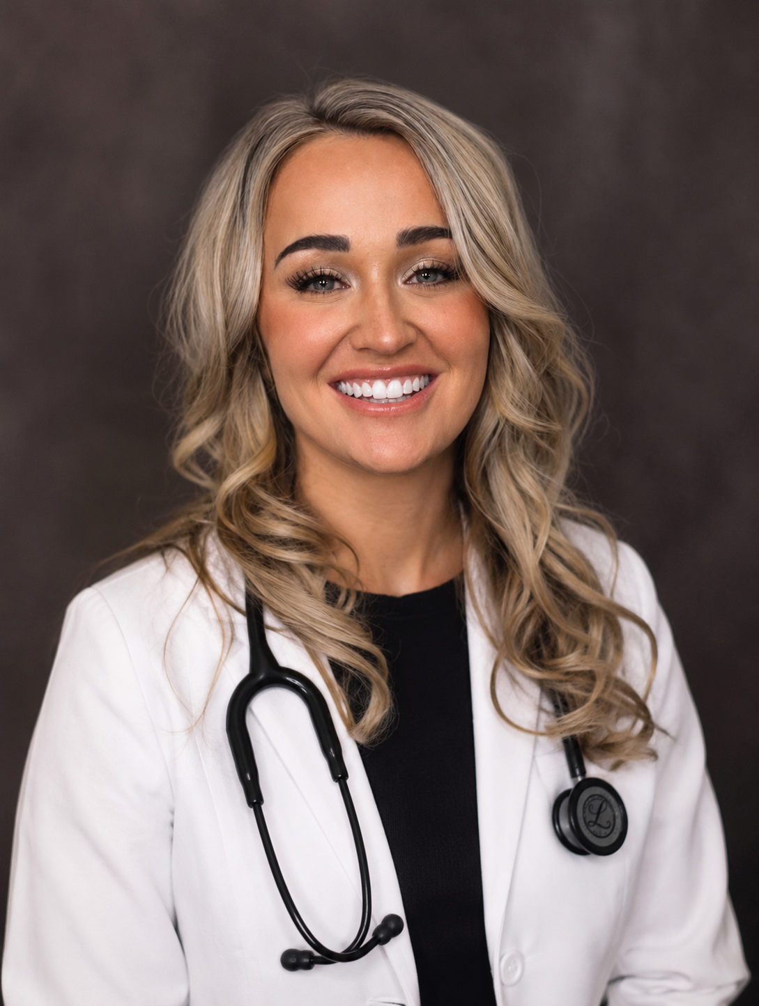 Smiling medical professional in white coat with stethoscope against a dark backdrop