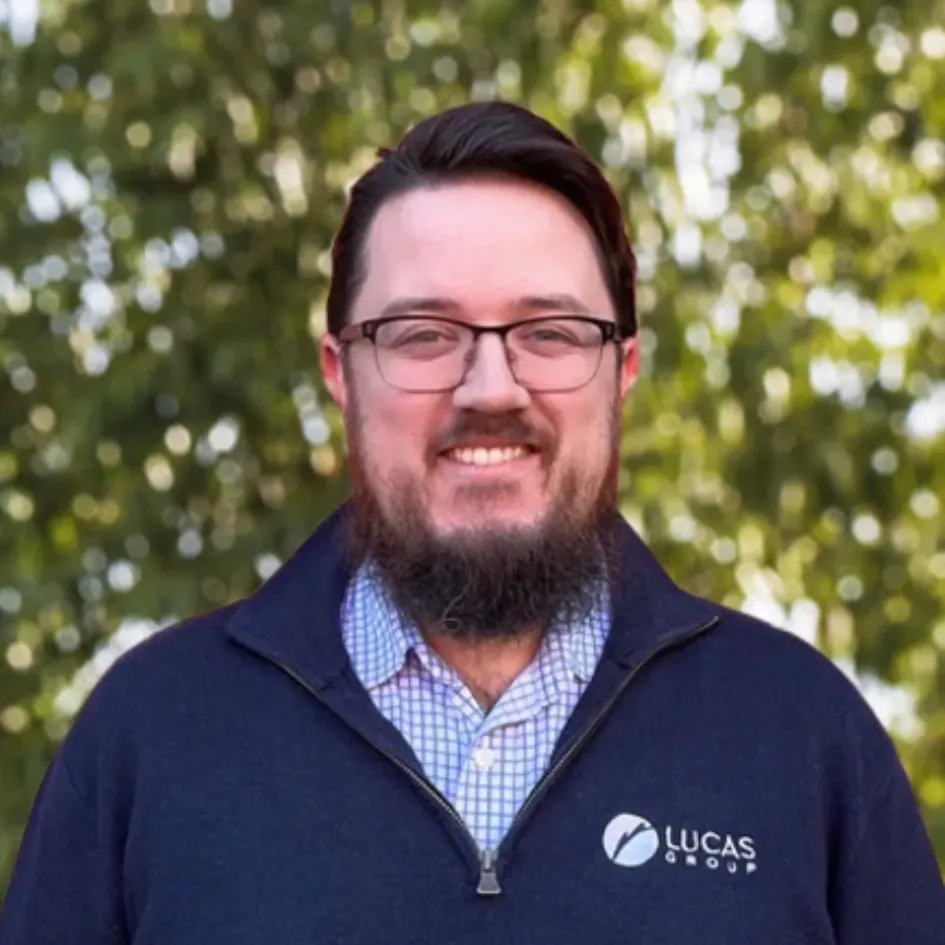 Man with glasses and beard smiles, wearing a navy blue sweater with