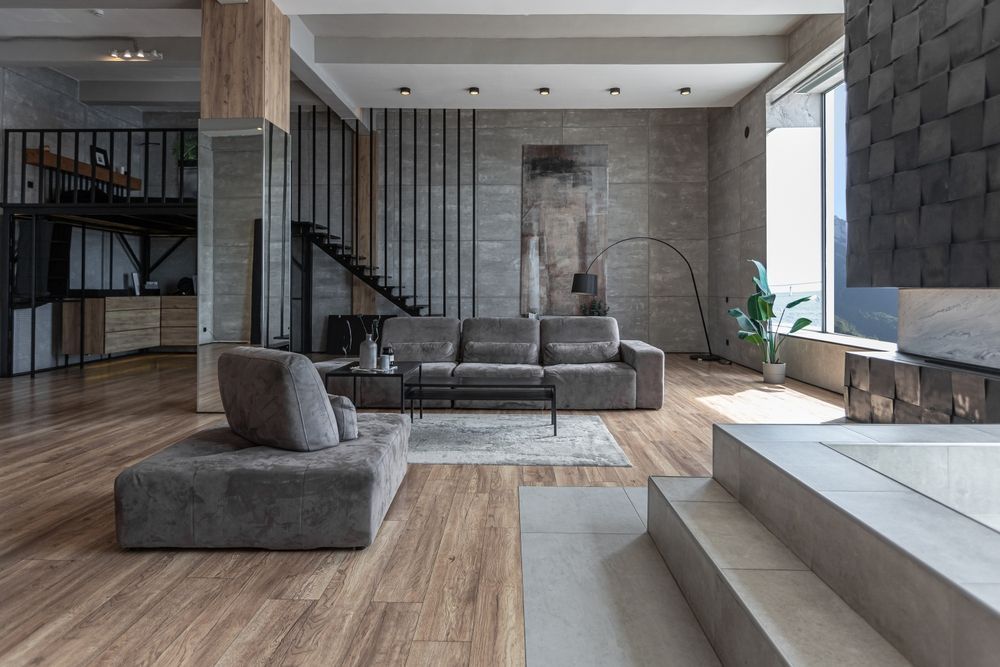 Modern living room with gray sofa, chair, and wood floors. Features a loft, stairs, and fireplace.