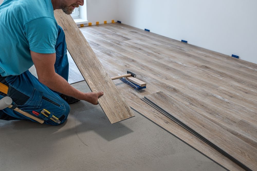 Man installing wood-look flooring indoors. He holds a plank, placing it next to other planks, with tools nearby.
