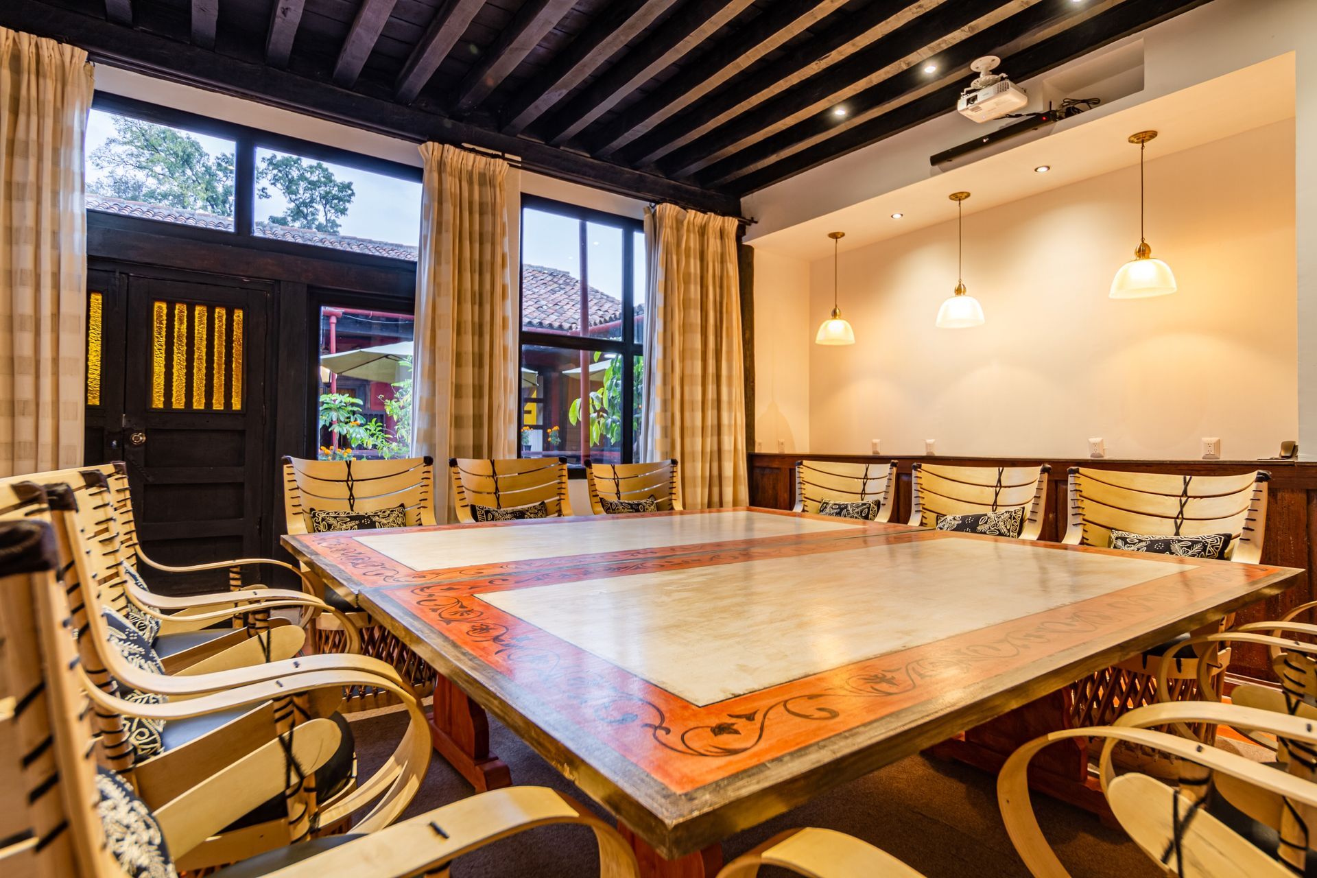 Conference room with long table and curved chairs, illuminated by hanging lights and natural light from windows.