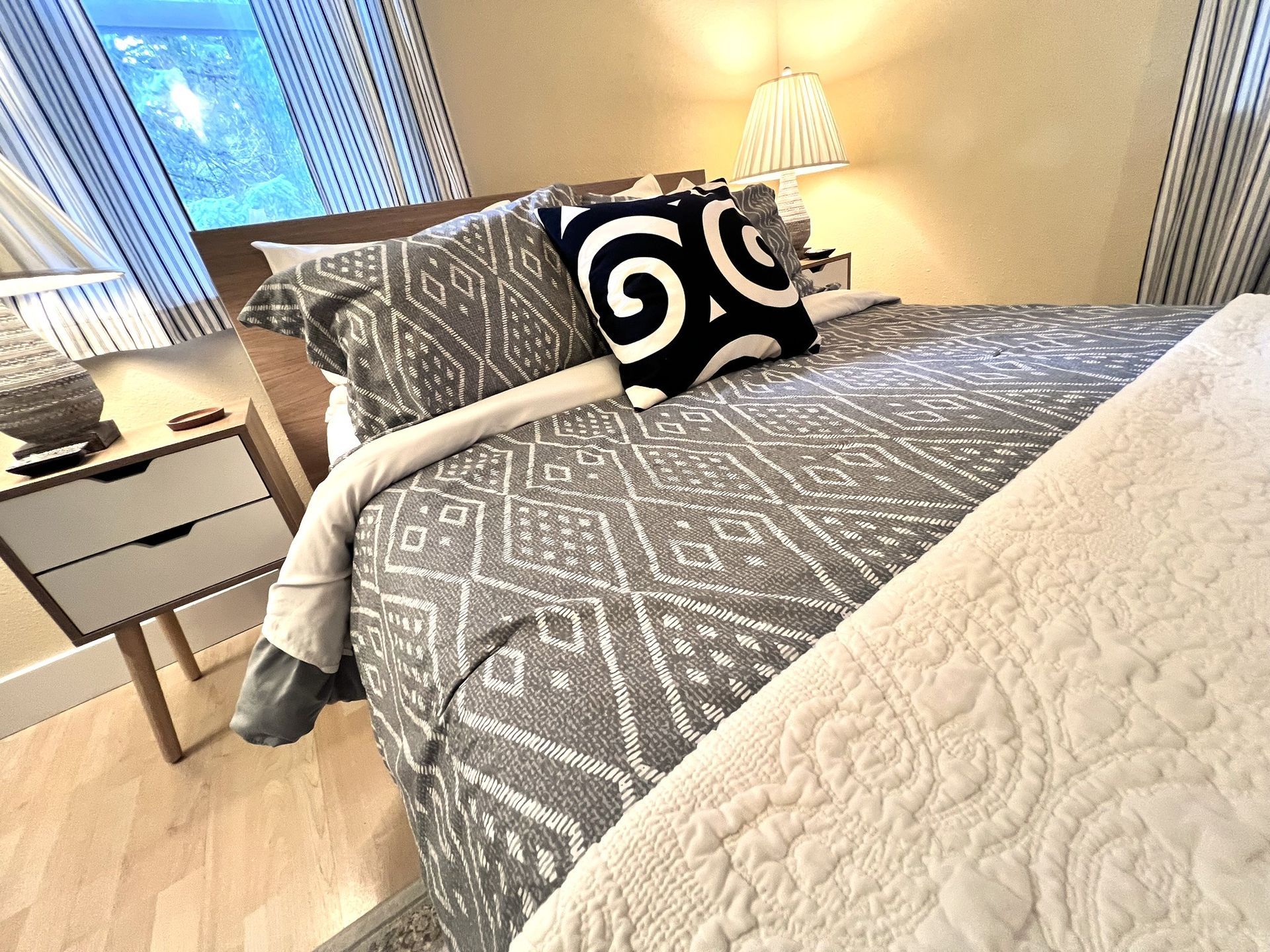 A bedroom with a bed , nightstand , lamp and window.