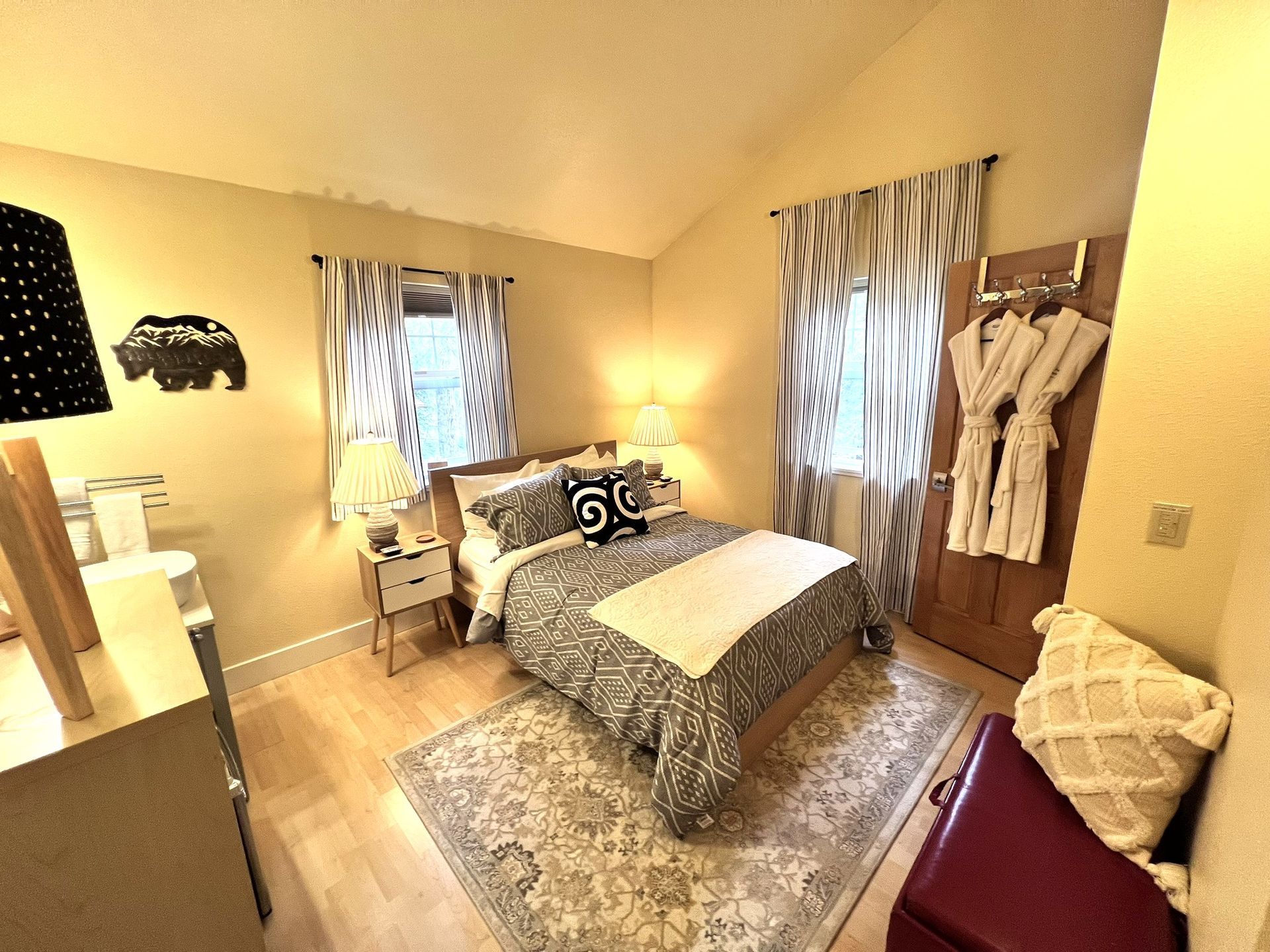 A bedroom with a bed , ottoman , nightstand , and window.