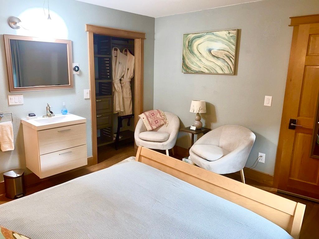 A bedroom with a bed , chairs , sink and mirror.