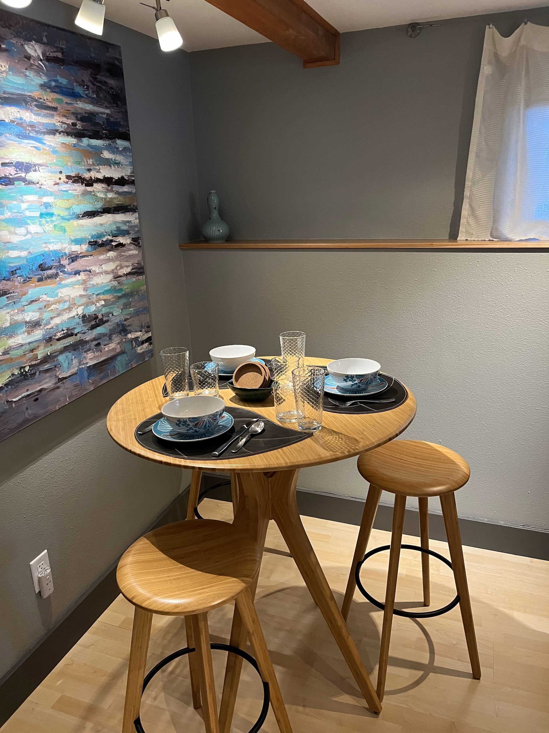 A dining room with a table and stools and a painting on the wall.