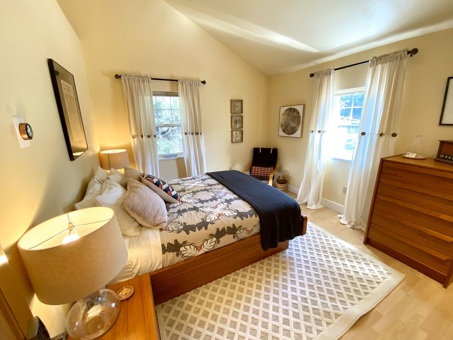A bedroom with a bed , dresser , nightstand , lamp and window.