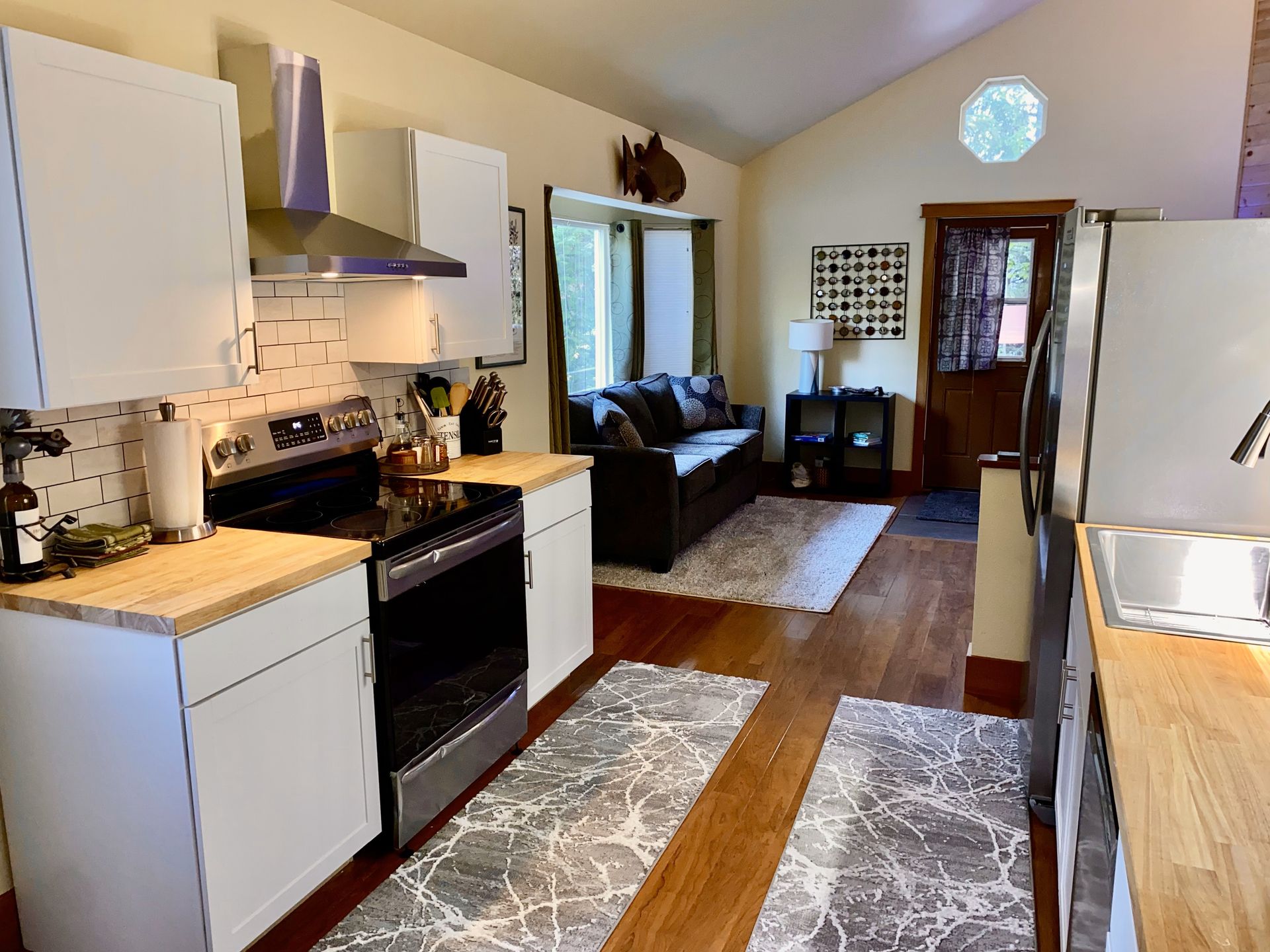 A kitchen with a stove , refrigerator , sink and a couch in the background.