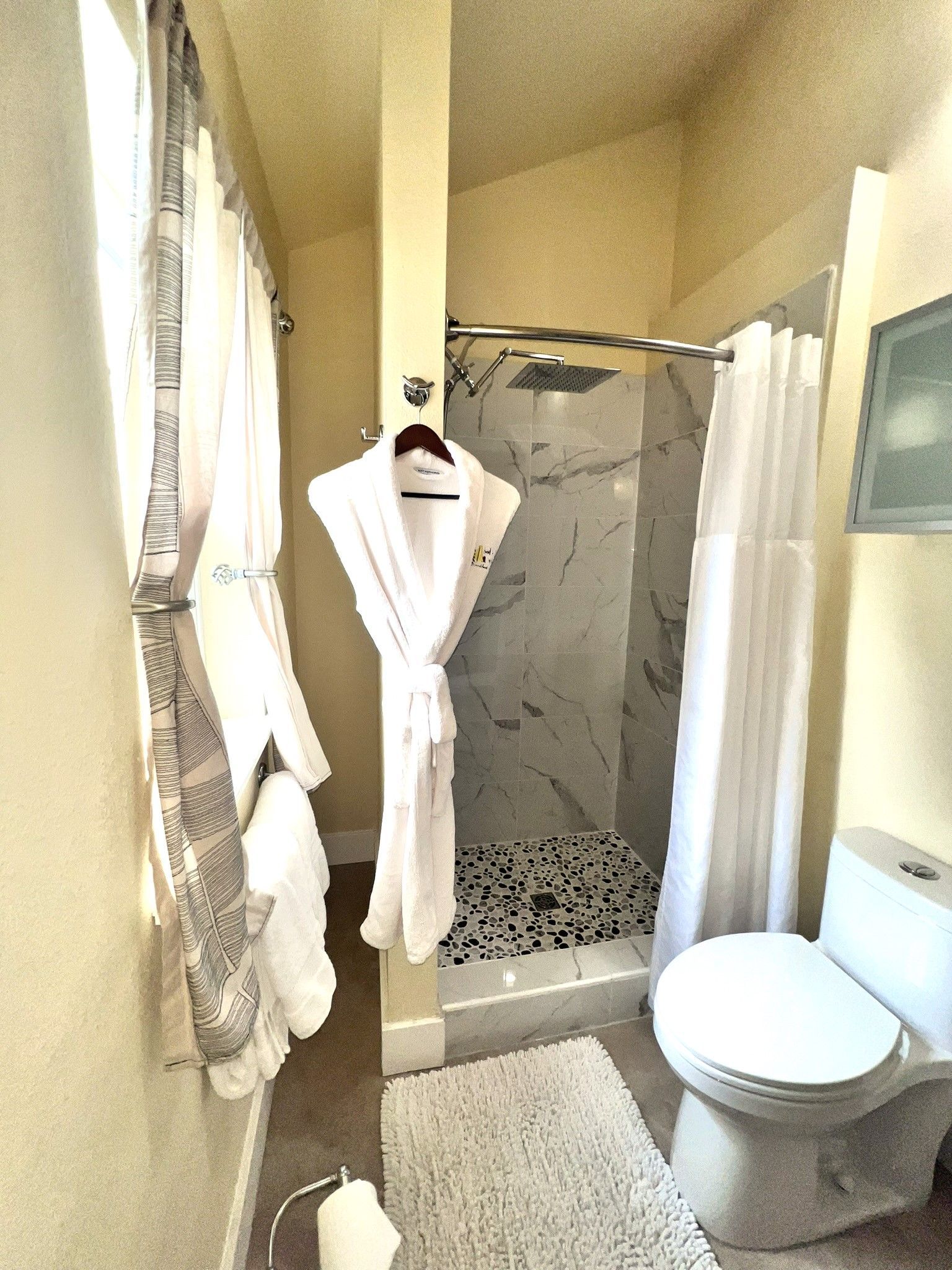 A bathroom with a toilet , shower , and robe hanging on the wall.