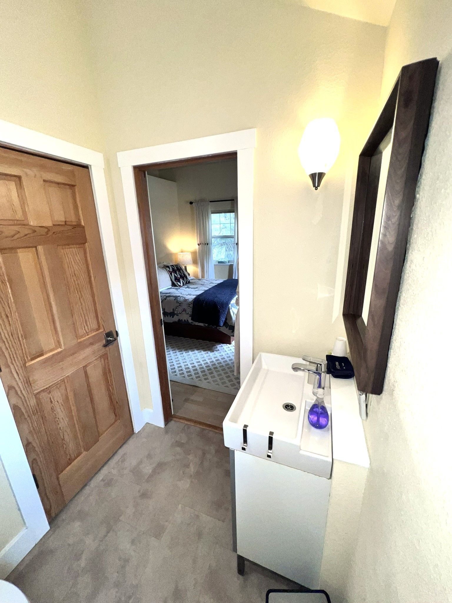 A bathroom with a sink , mirror and door leading to a bedroom.