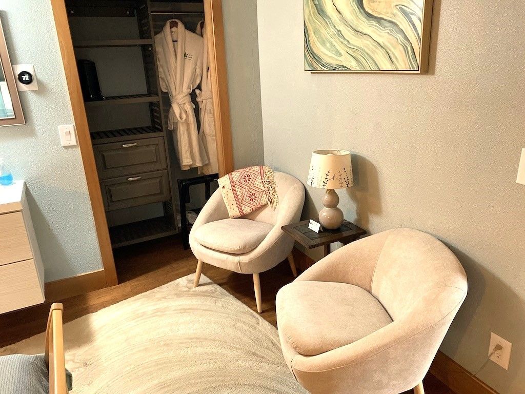 A bedroom with two chairs , a bed , a lamp and a closet.