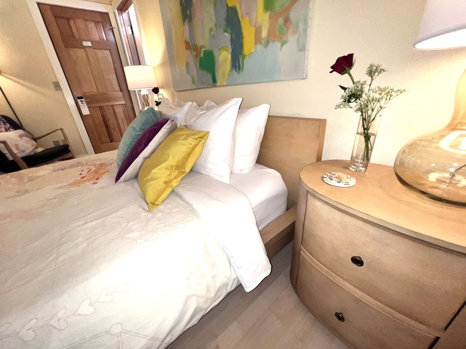 A bedroom with a bed and a nightstand with a vase of flowers on it