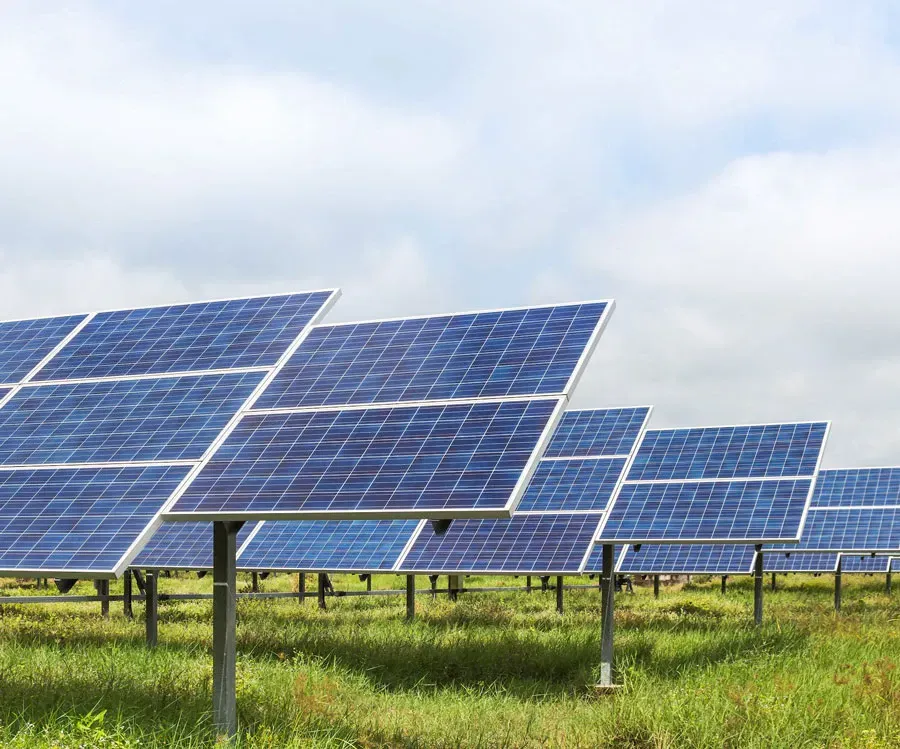 Rows of solar panels in a green field under a cloudy sky, capturing sunlight.