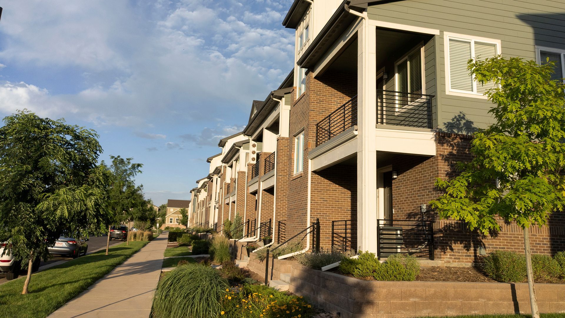 Row of modern townhouses with brick facades and white trim under a blue sky. 