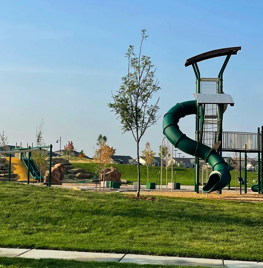 A playground with a winding green slide and climbing structure stands in Erie, CO.