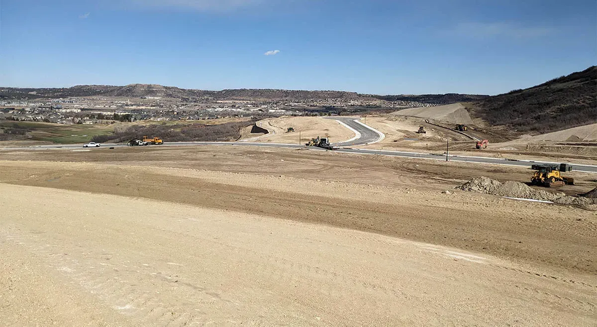 A construction site with a winding road, surrounded by barren land and hills.