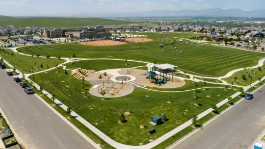 Aerial view of a sprawling park on a sunny day, showcasing a baseball field, playground, walking paths, and lush green lawns.