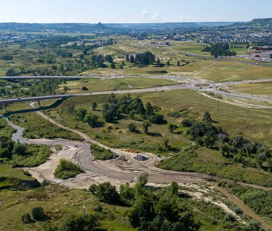 Aerial view of a lush green landscape with winding roads, roundabout, and a small river. 