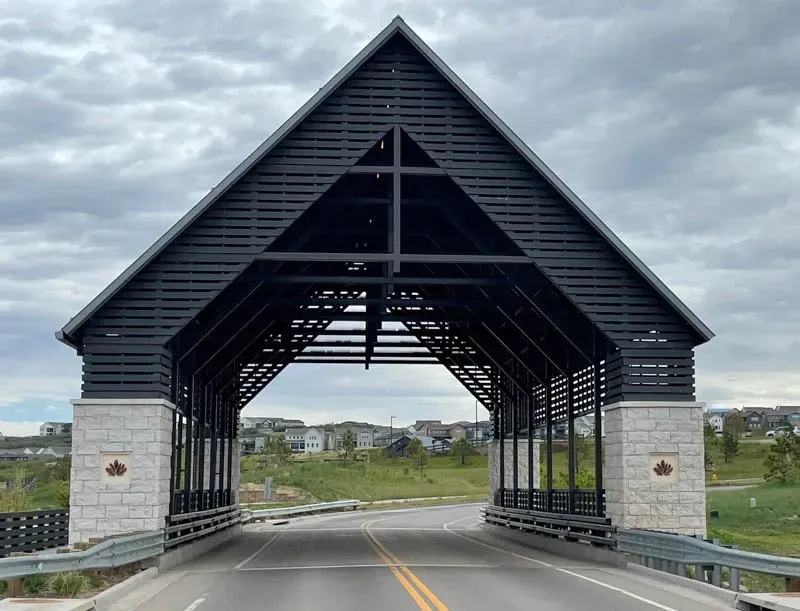 Modern covered bridge with metal roof and stone pillars over a winding road.