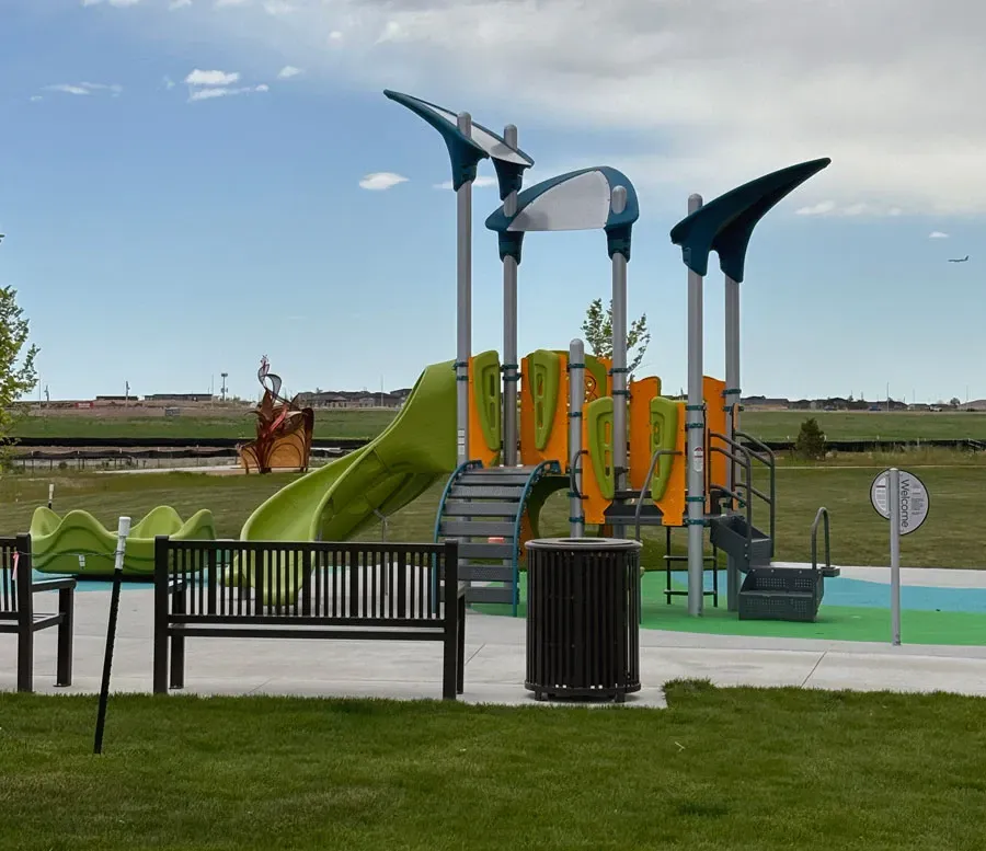 A colorful playground with green slides and climbing structures in Windy Plumes Park.