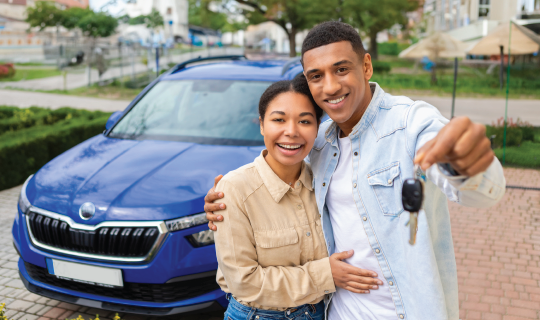 Couple smiling in front of a blue car; man holding car keys.