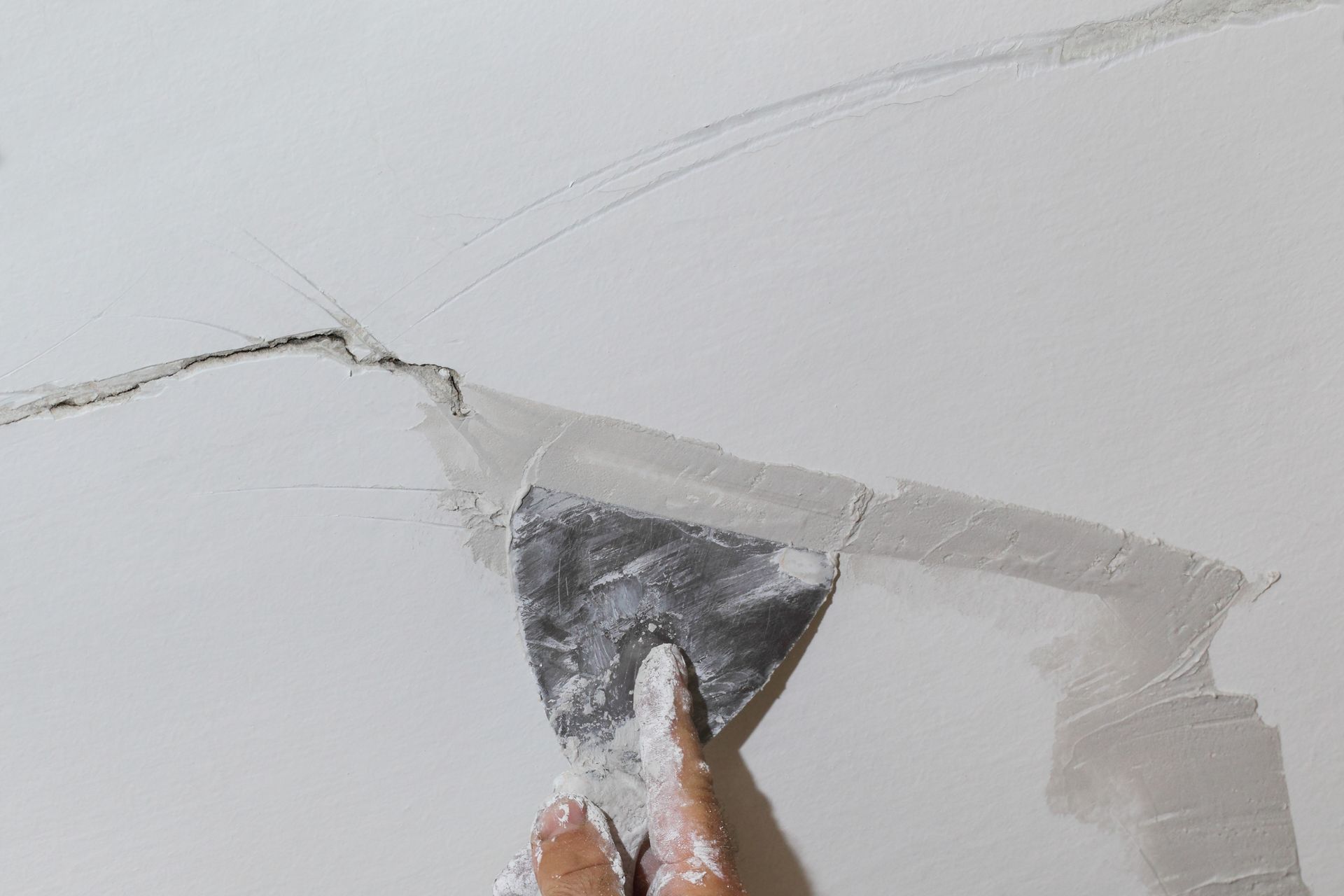 Hand using a trowel to apply drywall compound over a crack in a white wall.
