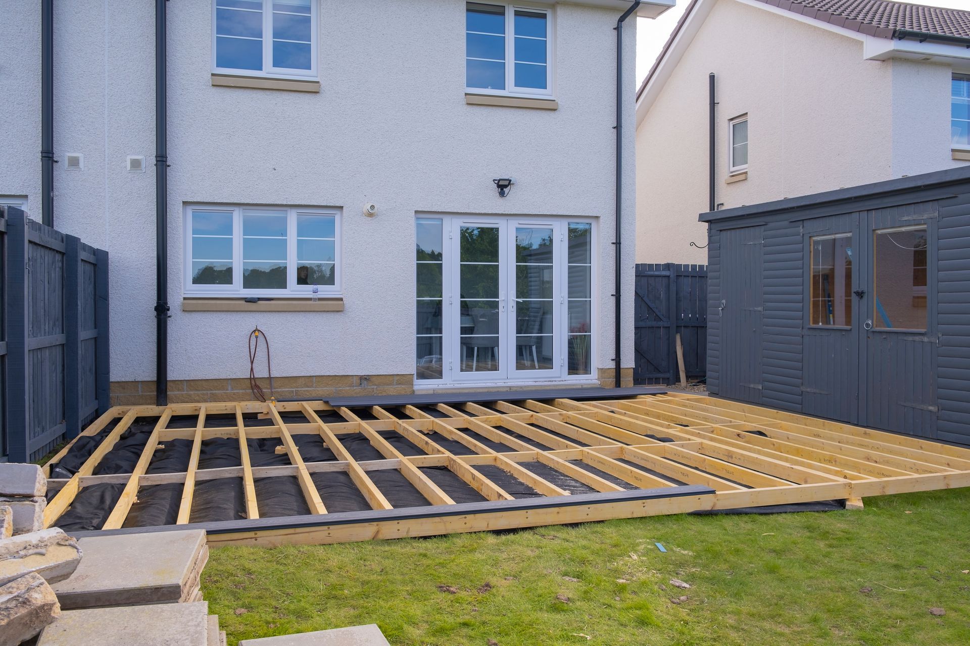 Backyard with a partially built wooden deck, next to a house and shed.