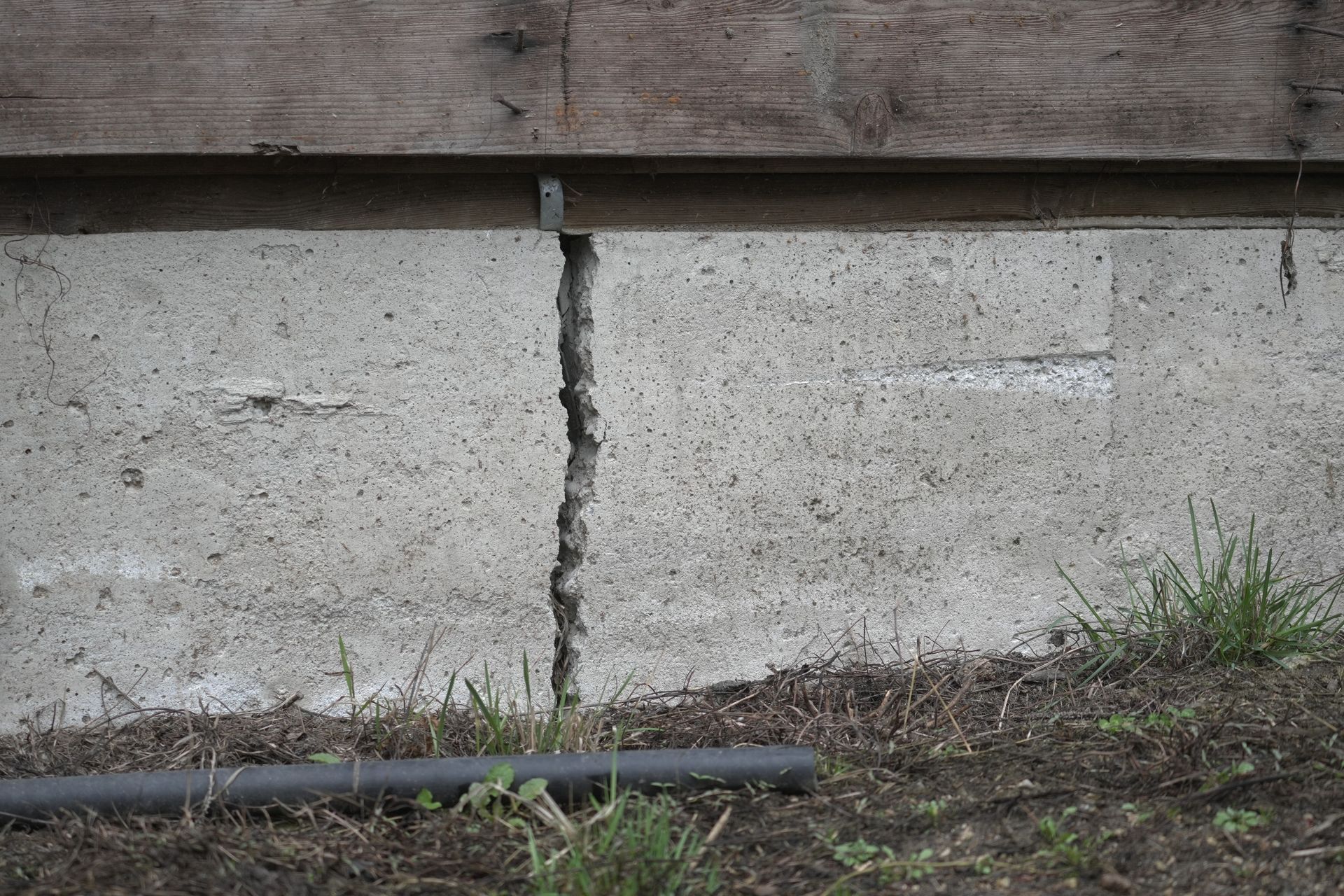 Cracked concrete foundation wall with wooden beam above; gray and brown exterior.
