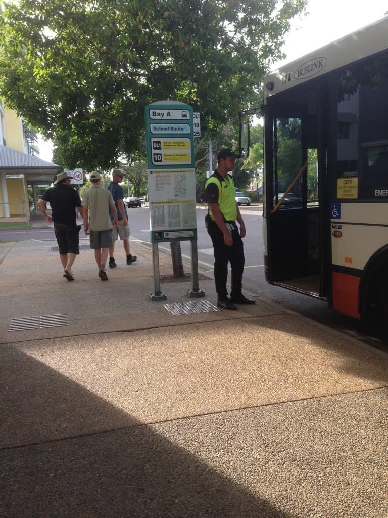 A Man In A Yellow Vest Is Standing Next To A Bus - Professional Security in Darwin, NT