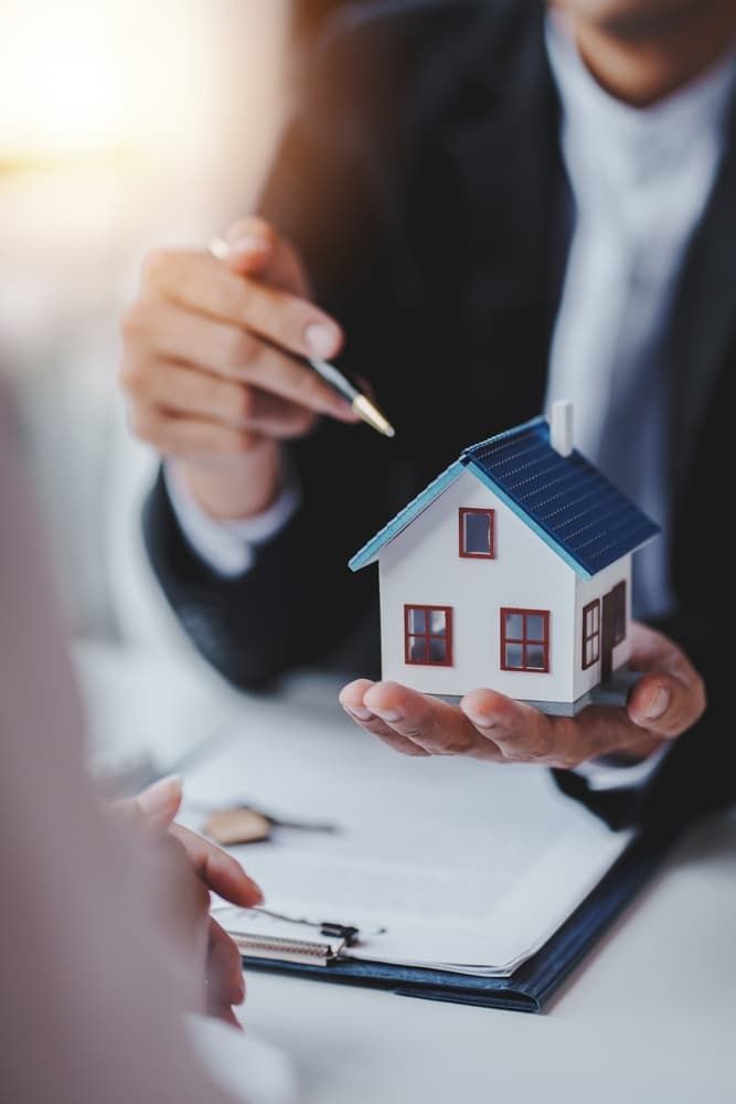 A Man Is Holding A Small Model House In His Hand - Professional Security in Darwin, NT