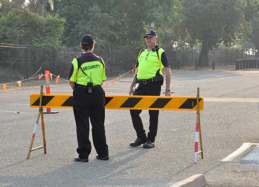 Two Security Guards Standing Behind A Yellow And Black Barrier - Security in the Top End, NT