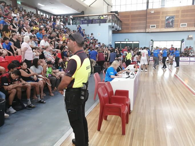 A Security Man Stands In Front Of A Crowd Of People Watching A Basketball Game - Professional Security in Darwin, NT