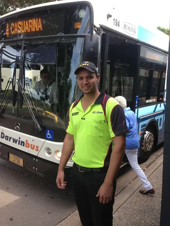 A Security Guard Standing Next To A Bus As A Pedestrian Walks On The Bu - Comprehensive Security Services in Darwin, NT