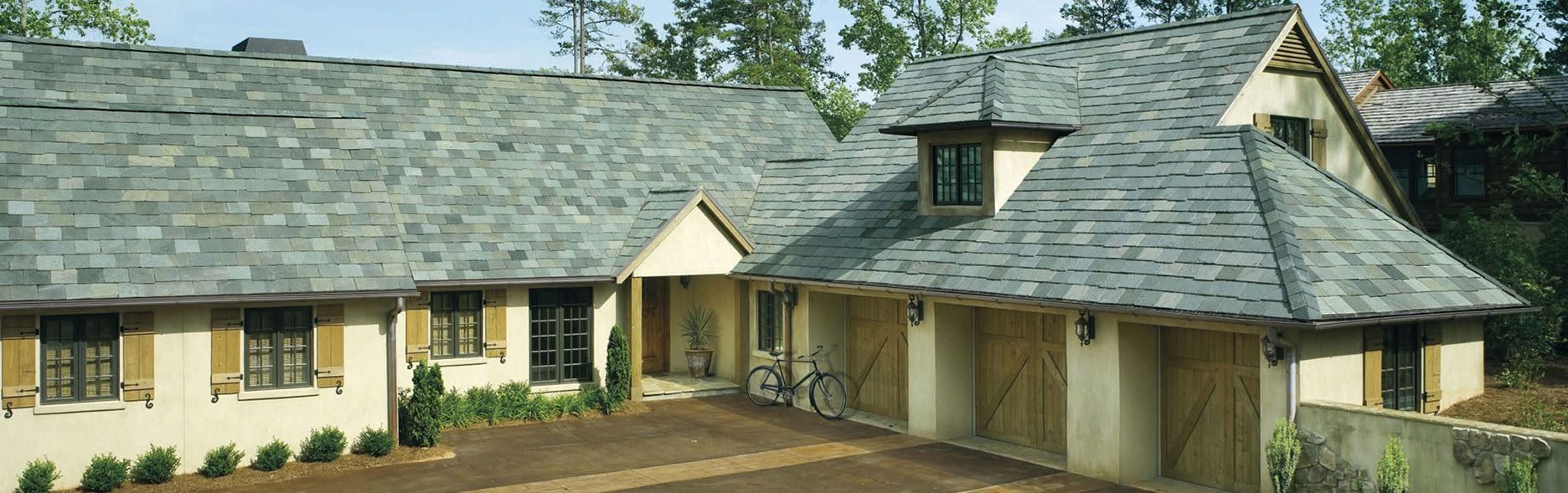 Single-story tan house with gray shingle roof and stone accents, set among trees and landscaping