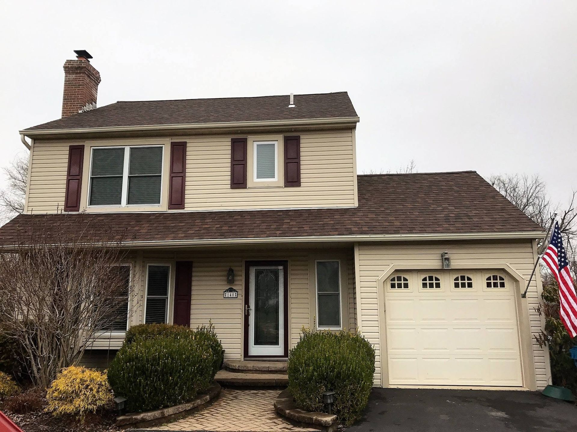 Two-story beige house with maroon shutters, garage, and a U.S. flag in the front yard
