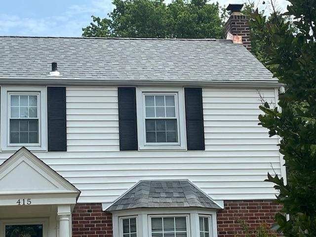 Two-story white house with black shutters, red brick lower facade, and gray roof shingles