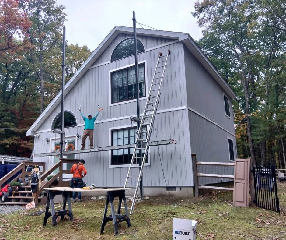 Workers painting a gray house exterior with ladders and scaffolding in a yard