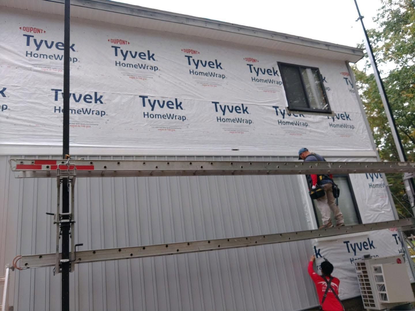 Workers on scaffolding install Tyvek wrap on a building under construction.