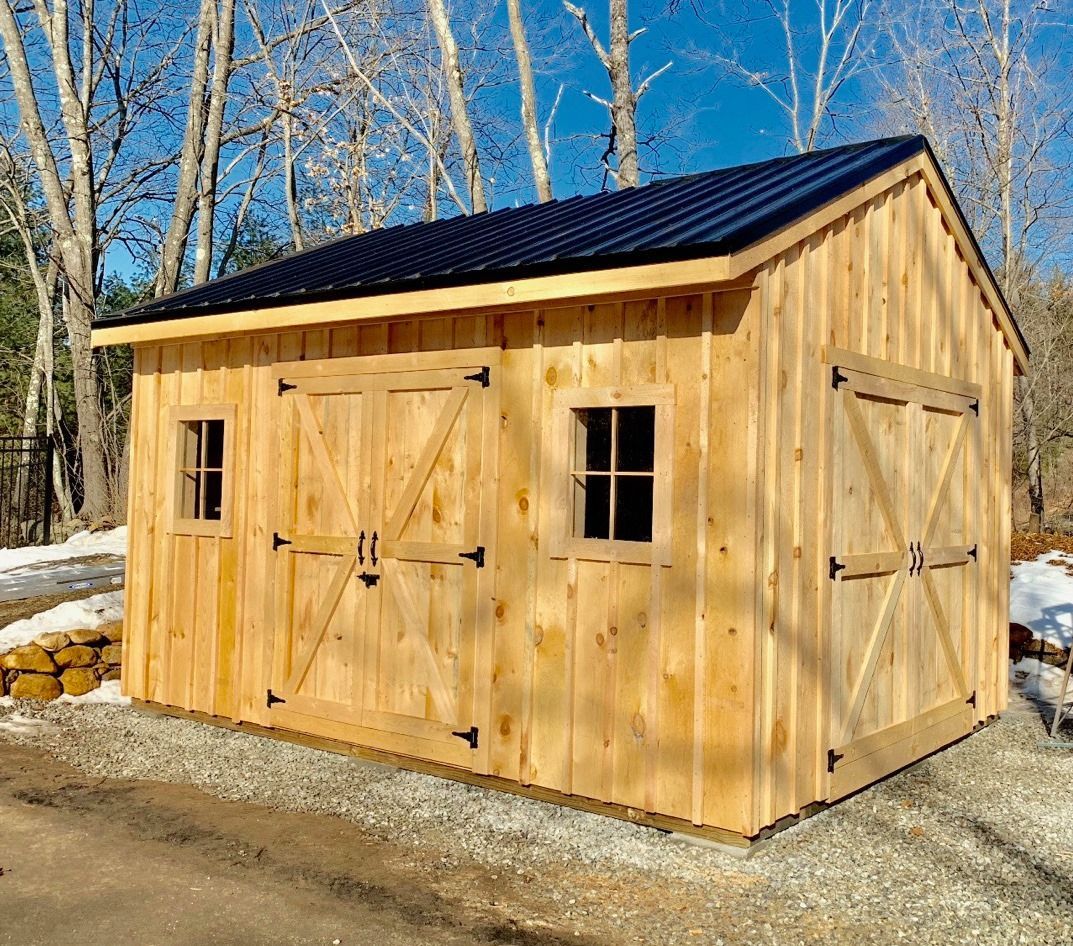 New wooden shed with double doors and two windows beside a snowy wooded area