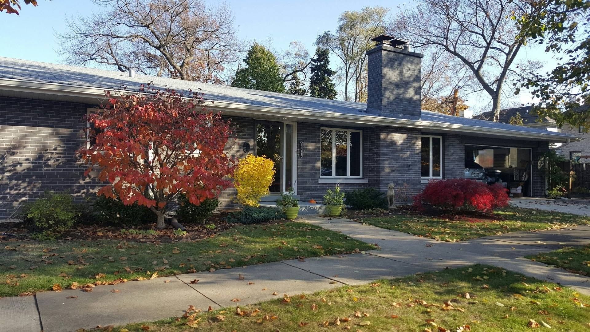 Single-story brick house with autumn trees, colorful shrubs, and a front walkway
