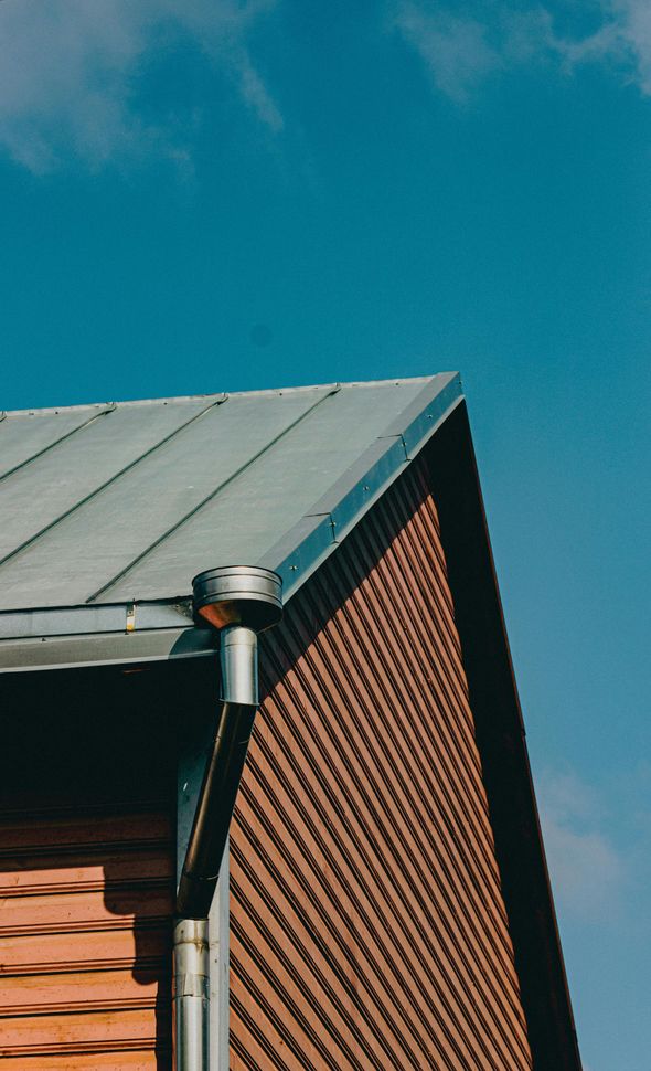Roof corner with metal gutter and downspout against a blue sky