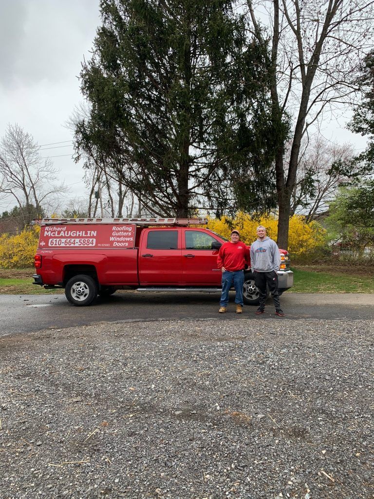 Three people standing by a red pickup truck on a gravel lot with trees in the background.