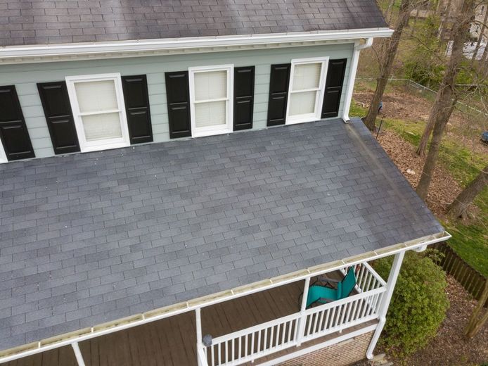 Aerial view of a house with a gray shingled roof, white porch railing, and black shutters.