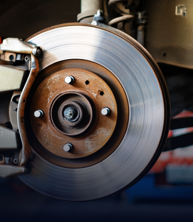 Close-up of a car brake rotor and caliper in a workshop, showing metal disc and hub.