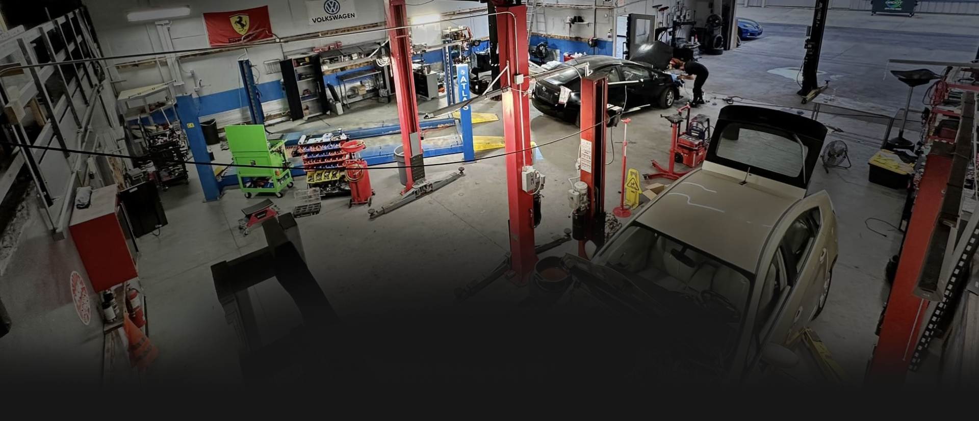 Auto repair shop with a raised car, red lifts, and tools scattered across the garage floor.