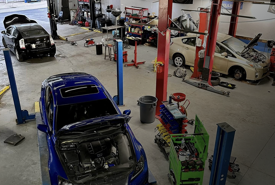 Auto repair shop with several cars on lifts and a blue car in the foreground