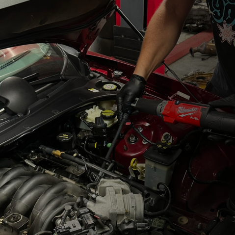 Car with hood open in an auto repair shop, showing the engine bay and tools in the background
